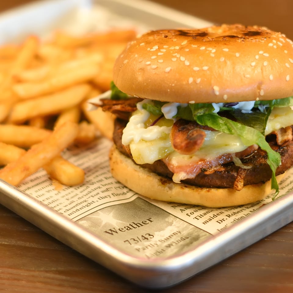 A juicy burger with melted cheese, bacon, and lettuce, served with golden fries on a metal tray.
