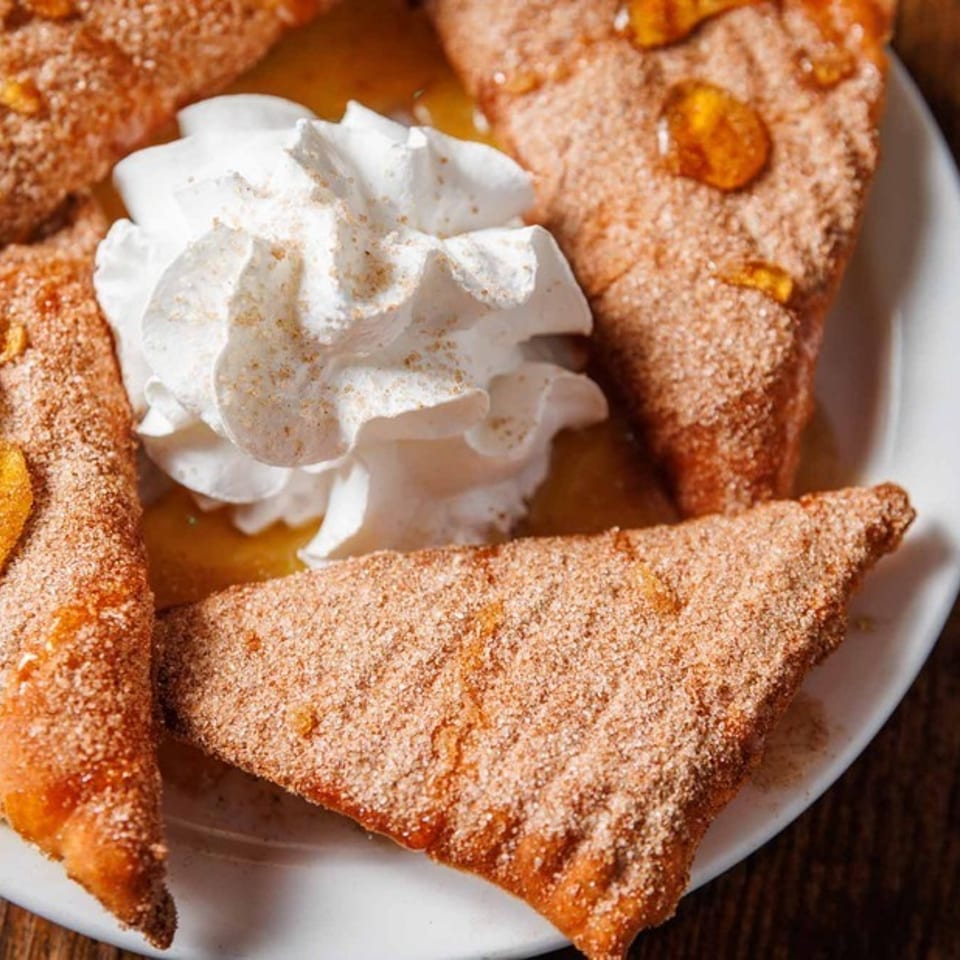 Four triangular pastries dusted with cinnamon sugar, drizzled with honey, and topped with whipped cream.