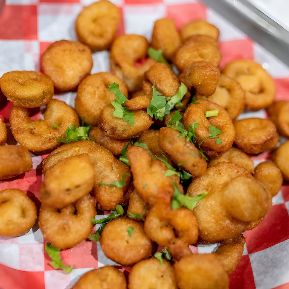 Golden brown fried seafood pieces, some round and some ring-shaped, garnished with cilantro on a red and white checkered paper.