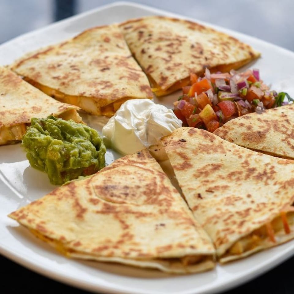 A white plate with six quesadilla wedges, guacamole, sour cream, and pico de gallo.