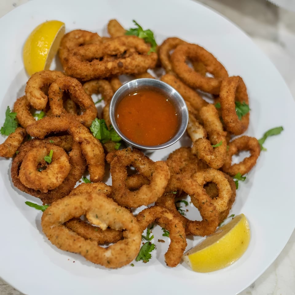 Crispy fried calamari rings and tentacles with a side of red dipping sauce and lemon wedges.