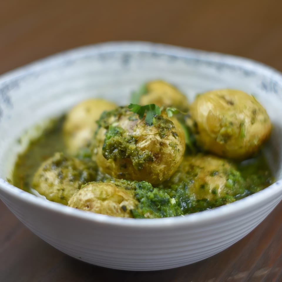 Small, golden potatoes covered in a vibrant green pesto sauce, served in a white bowl.