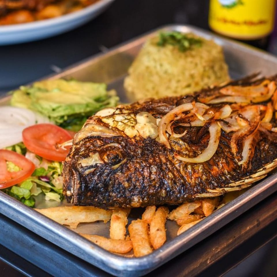 Whole fried fish with onions, rice, fries, avocado, salad, and lime on a metal tray.