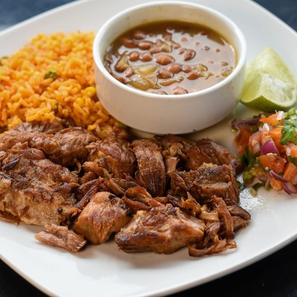 A plate of carnitas with rice, beans, pico de gallo, and a lime wedge.