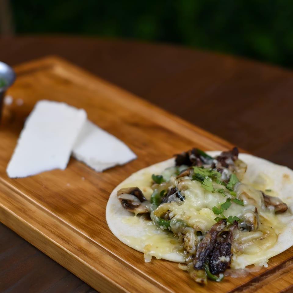 Mushroom and cheese taco with cilantro, served on a wooden board with white cheese and green sauce.