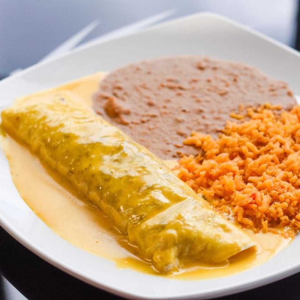 A plate of Mexican food with a green chile enchilada, refried beans, and orange rice.