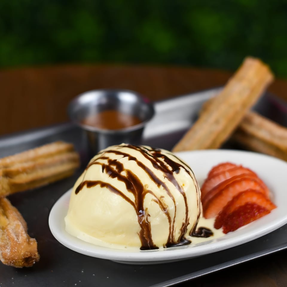 Vanilla ice cream with chocolate drizzle, sliced strawberries, churros, and caramel sauce on a tray.