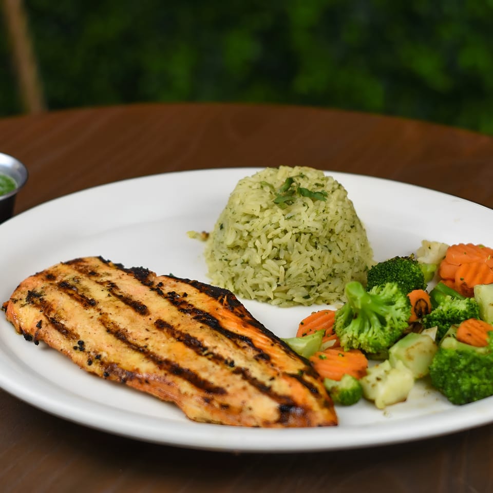 Grilled chicken breast with green rice, steamed broccoli, carrots, and two small sauce cups.