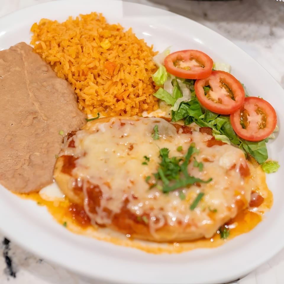A white plate with a cheesy enchilada, refried beans, orange rice, and a side salad.