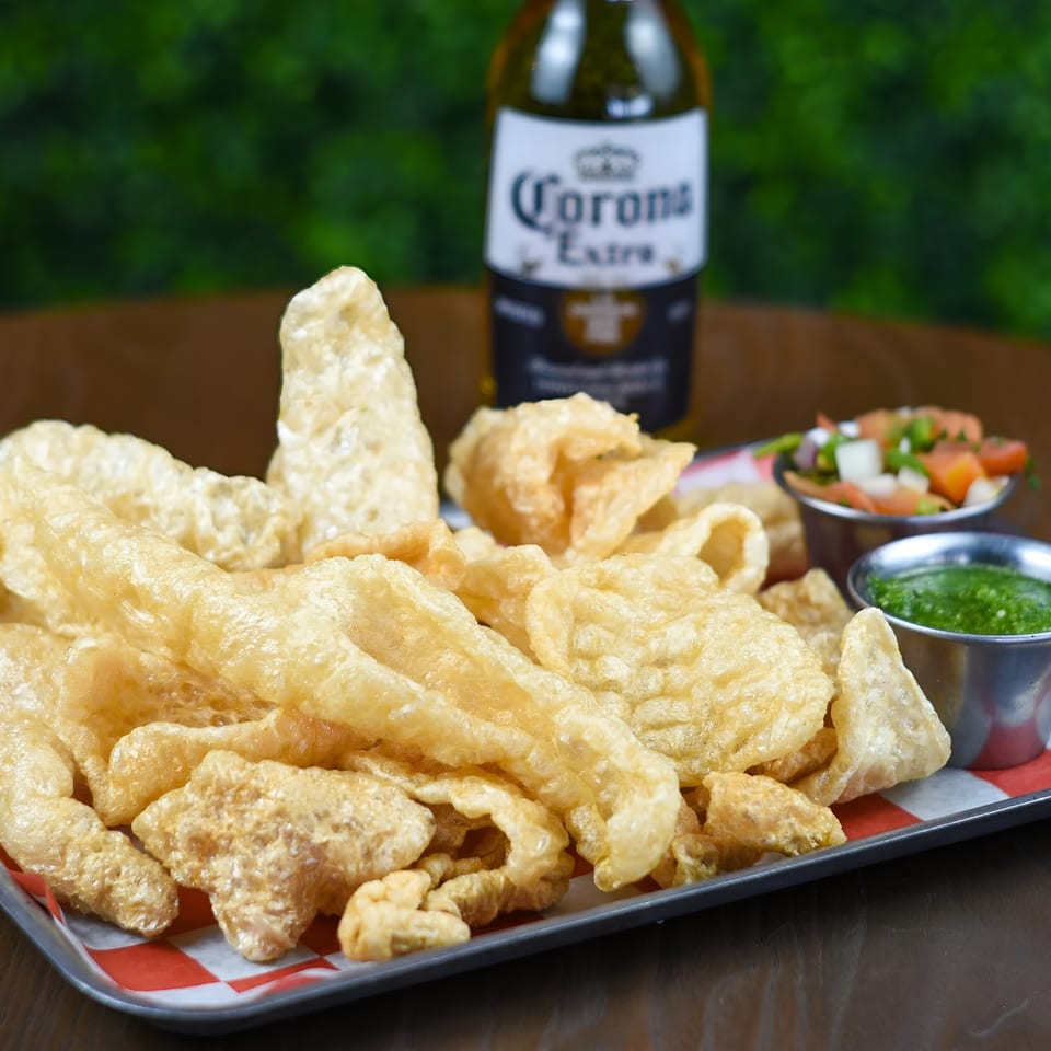 Crispy chicharrones on a tray with salsa and pico de gallo, and a Corona beer.