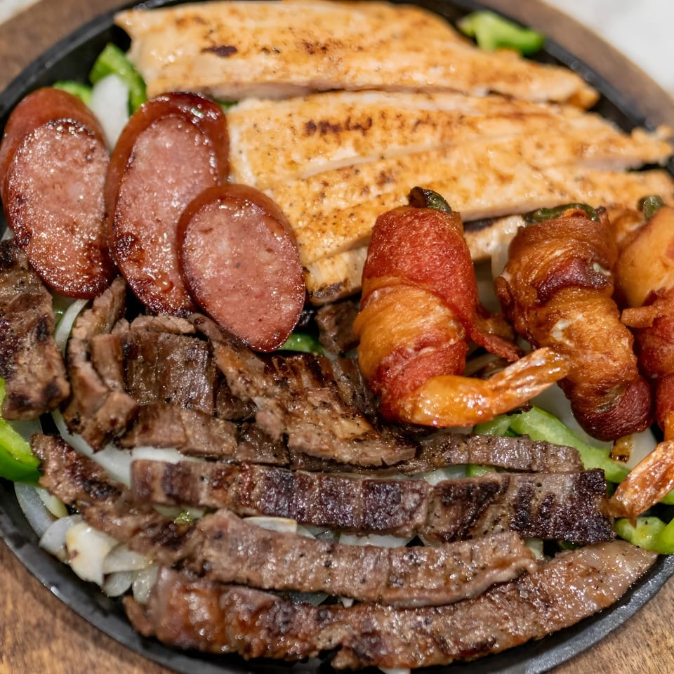 Sizzling fajita platter with steak, chicken, sausage, bacon-wrapped shrimp, onions, and peppers.