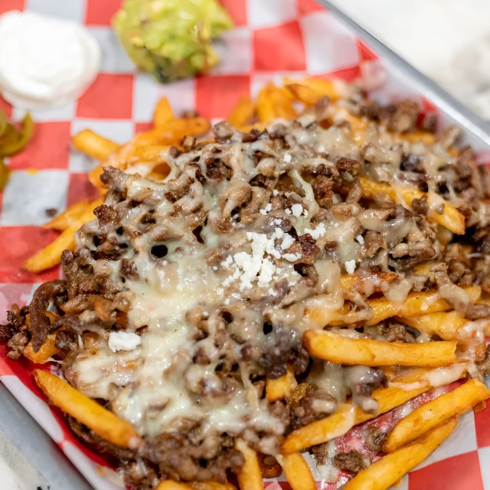 Loaded fries with melted cheese, ground meat, and a side of jalapeños, sour cream, and guacamole.