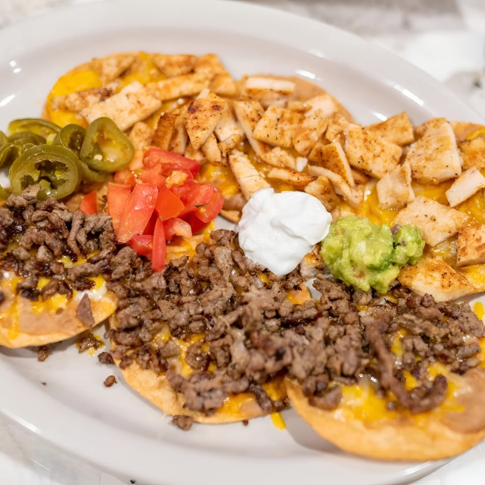 A plate of nachos with ground beef, chicken, jalapeños, tomatoes, sour cream, and guacamole.