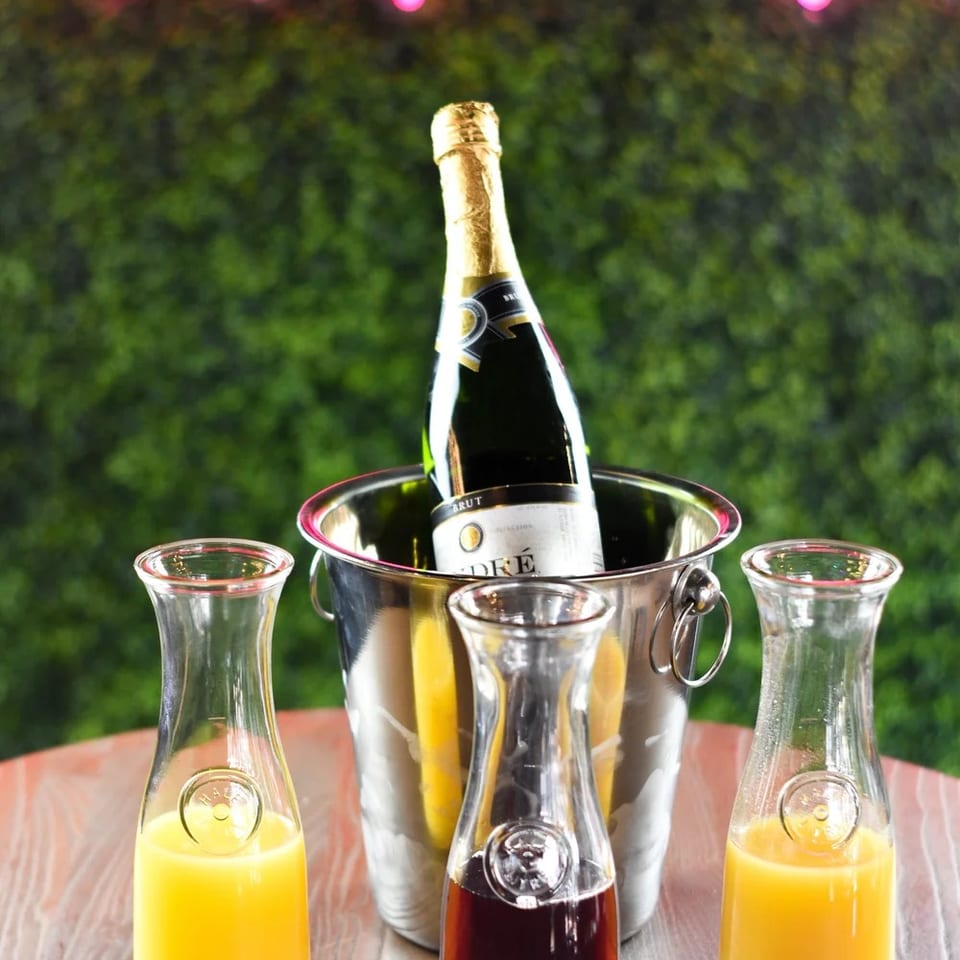 Champagne bottle in an ice bucket with three carafes of juice on a wooden table.